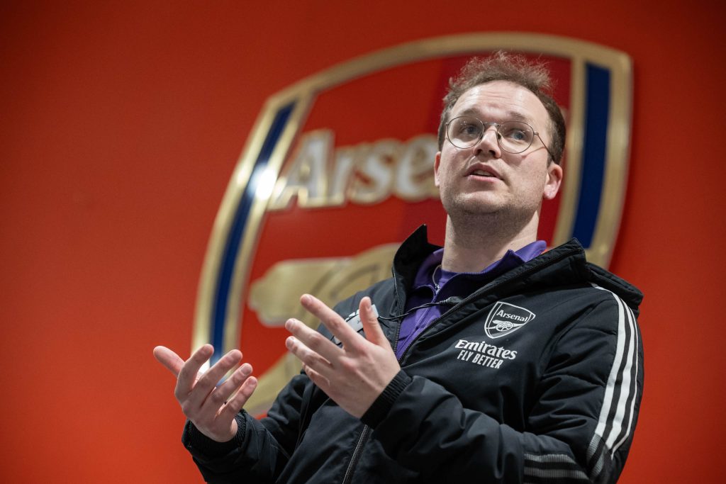 Speaker in Arsenal jacket presenting during a corporate event at the Emirates Stadium, captured by Jolley Productions