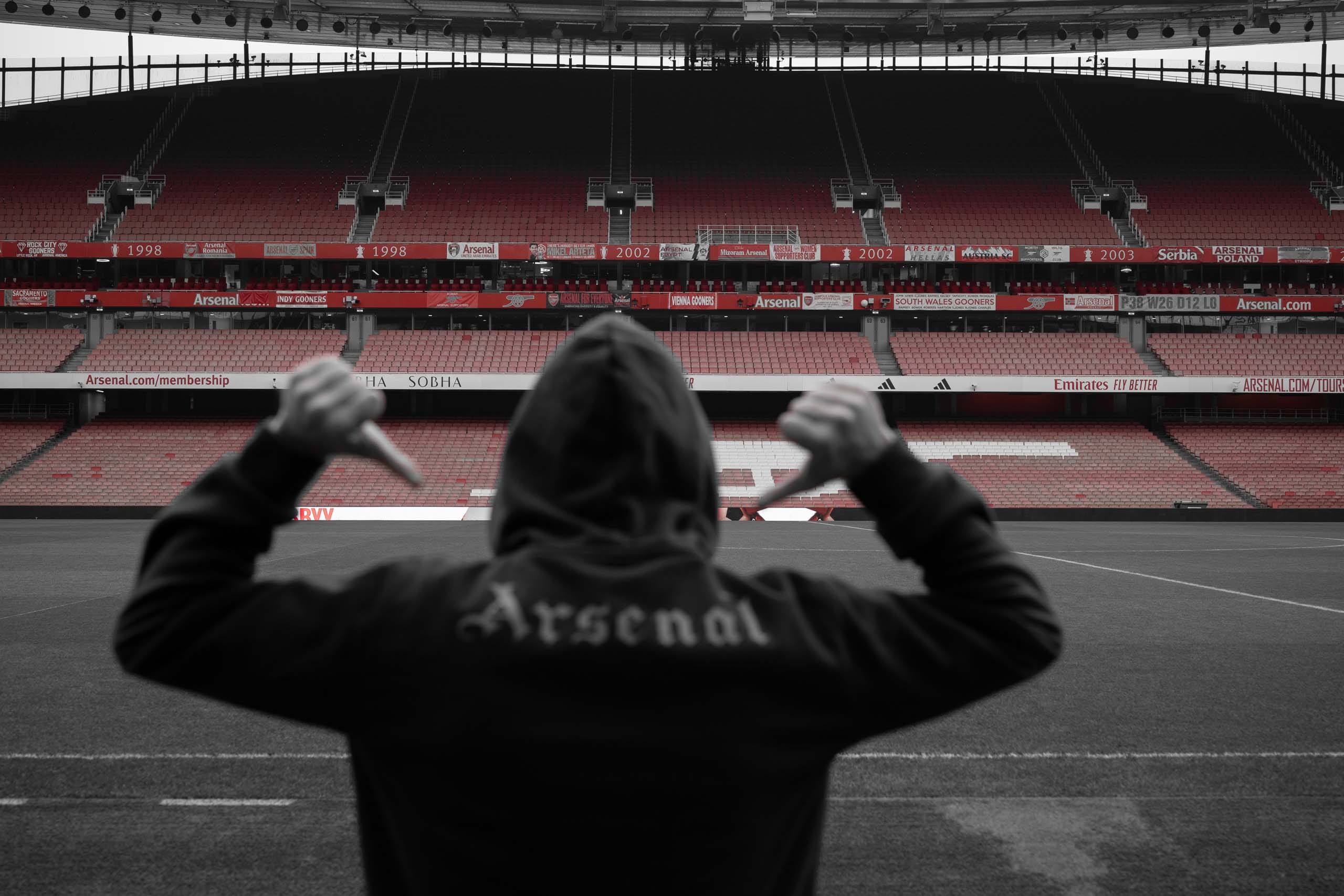 Football fan in hoodie celebrates on the pitch at Arsenal’s Emirates Stadium, captured from behind by Jolley Productions