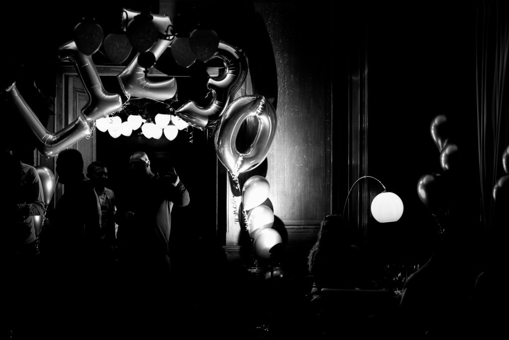 Black and white photo with large 30 balloons and silhouettes of guests at a dark indoor party venue.