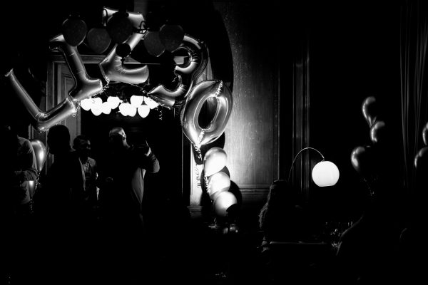 Black and white photo with large 30 balloons and silhouettes of guests at a dark indoor party venue.