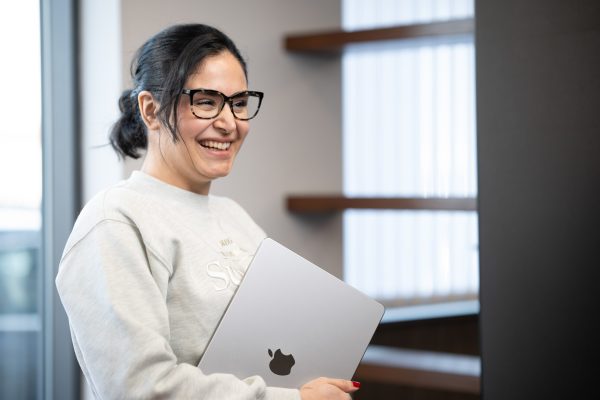 Woman in glasses smiling while holding a MacBook in a bright office space, captured by Jolley Productions during a relaxed team shoot
