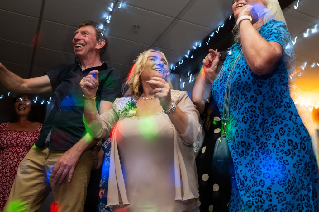 Energetic moment of a group of adults dancing indoors, lit with fairy lights and colourful disco effects.