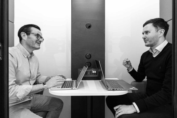 Black and white photo taken from a corporate video of two men in a meeting booth.