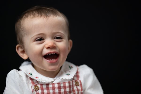 A baby is laughing in a red and white gingham with a black background.