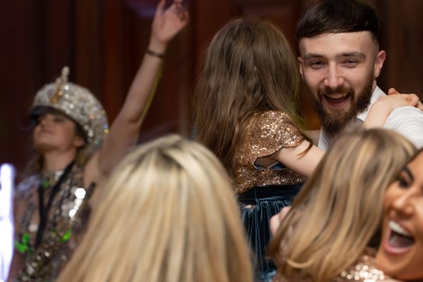 A bearded man in a white shirt holding a young girl dressed in glitter, smiling together while dancing at a party.