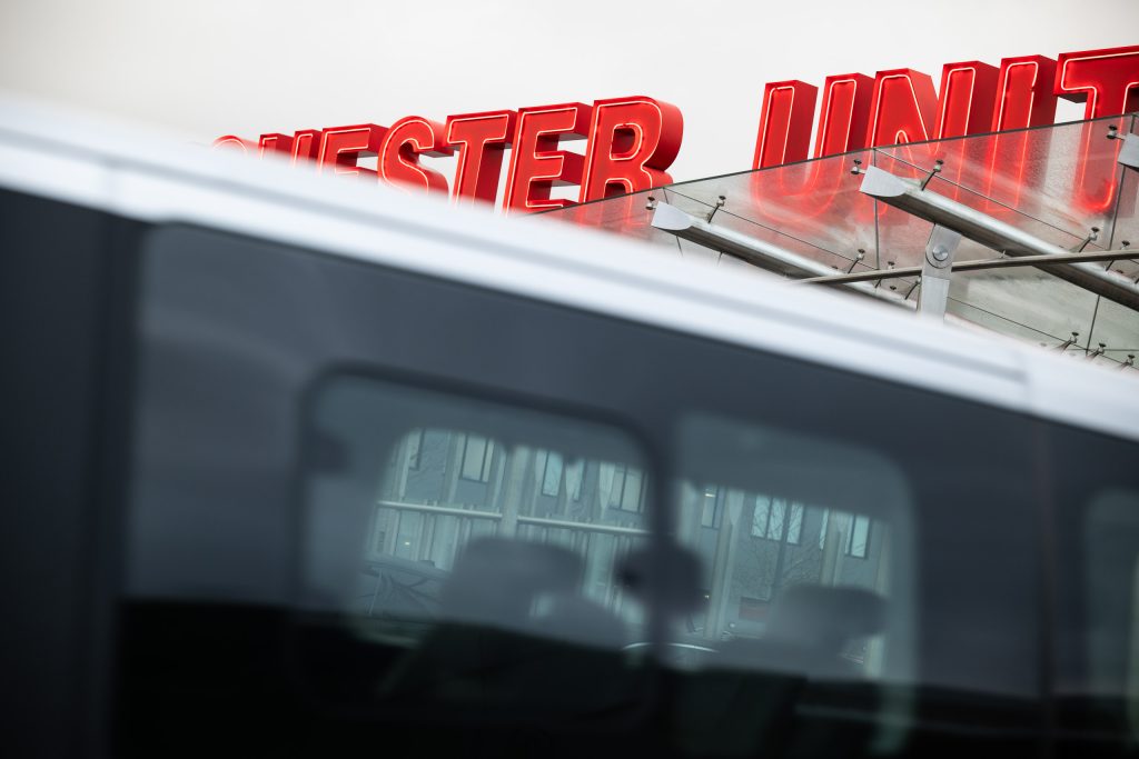 Striking shot of Manchester United’s red stadium signage with a minibus in the foreground, photographed by Jolley Productions for marketing use