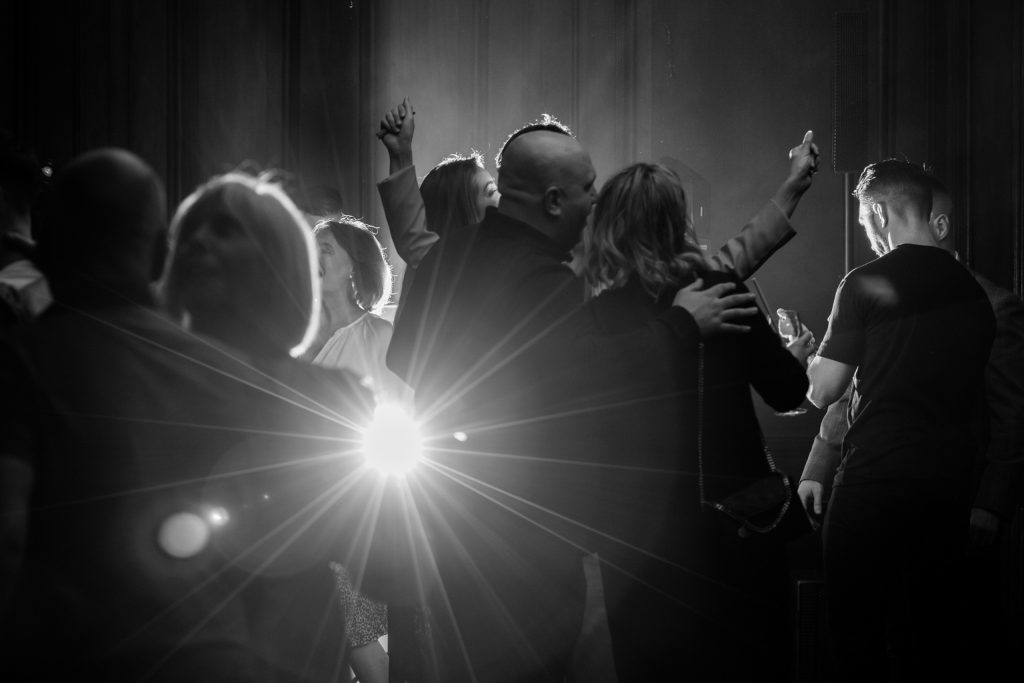 Black and white photo of a packed dancefloor lit dramatically by a burst of light, capturing silhouettes mid-celebration.