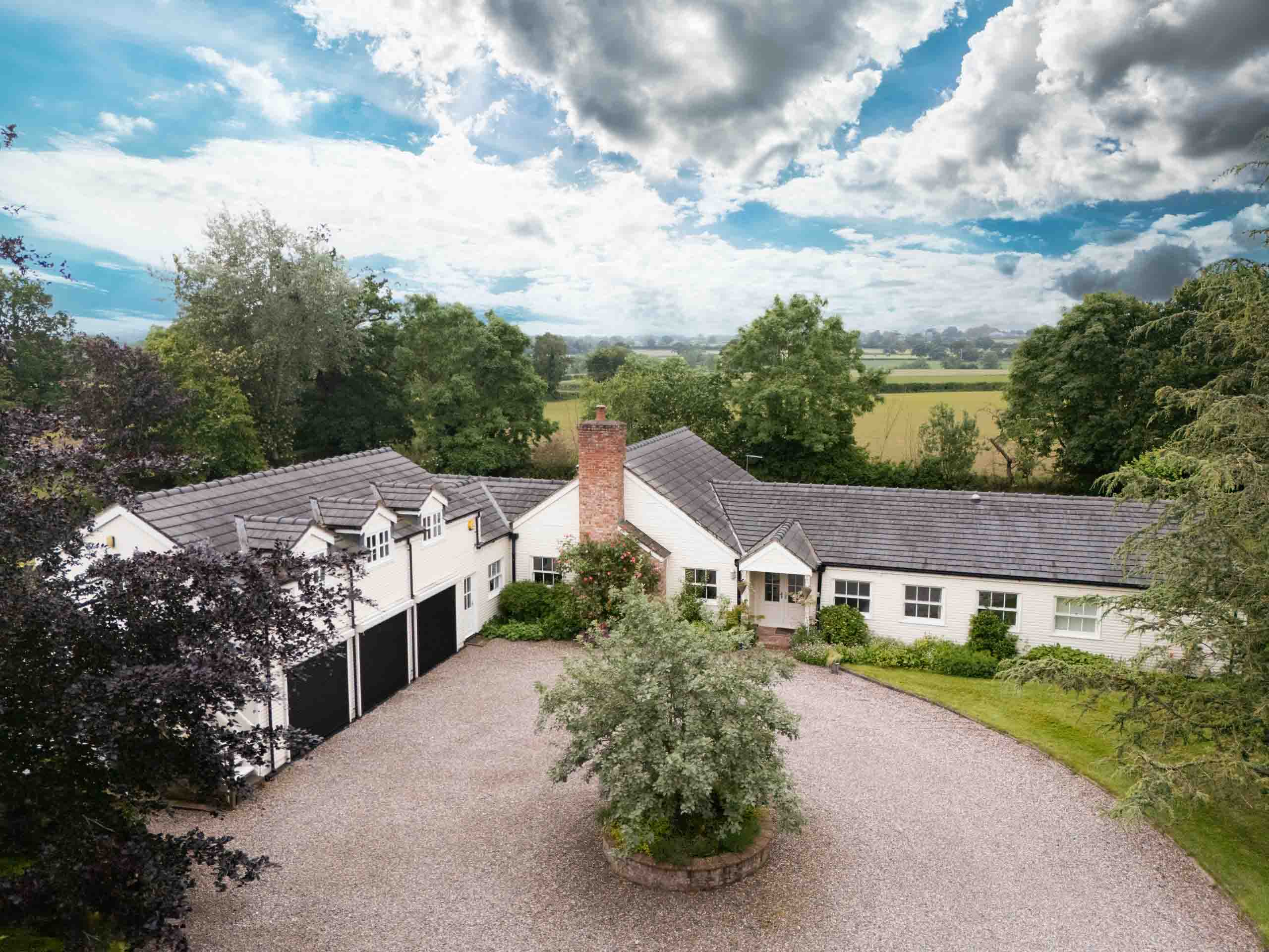 Long white-painted country house with circular gravel driveway and surrounding fields.