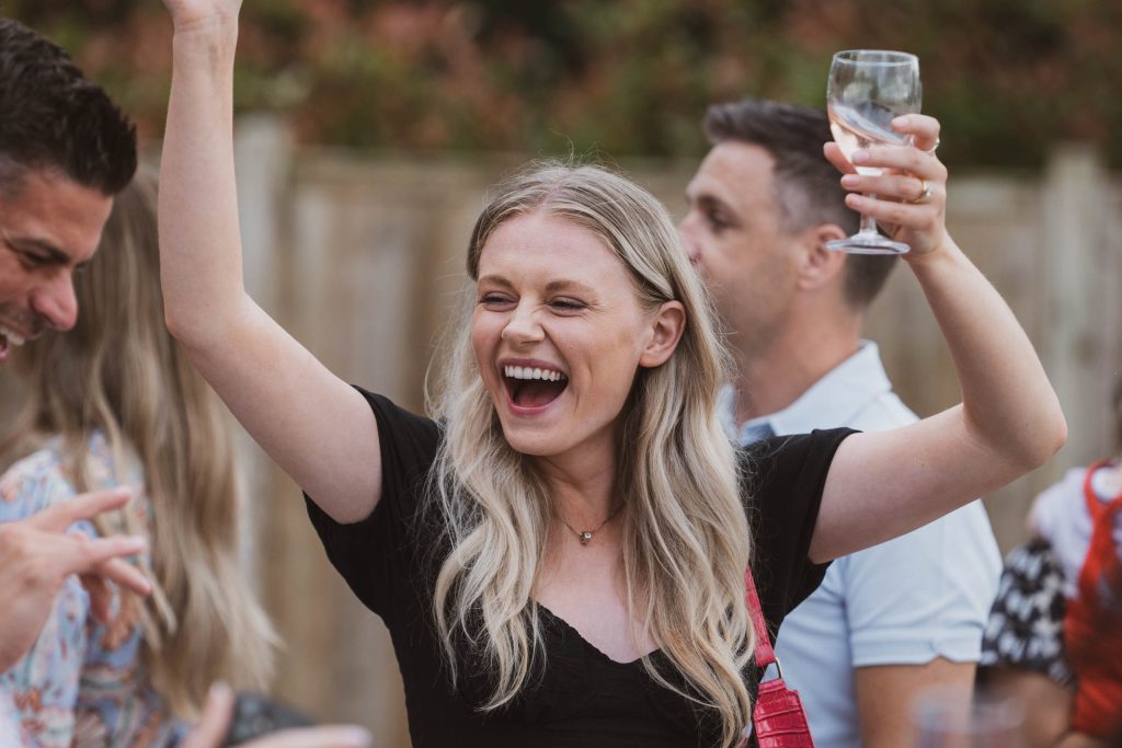Candid image of a woman in a black dress cheering with a glass of wine among friends at an outdoor party.