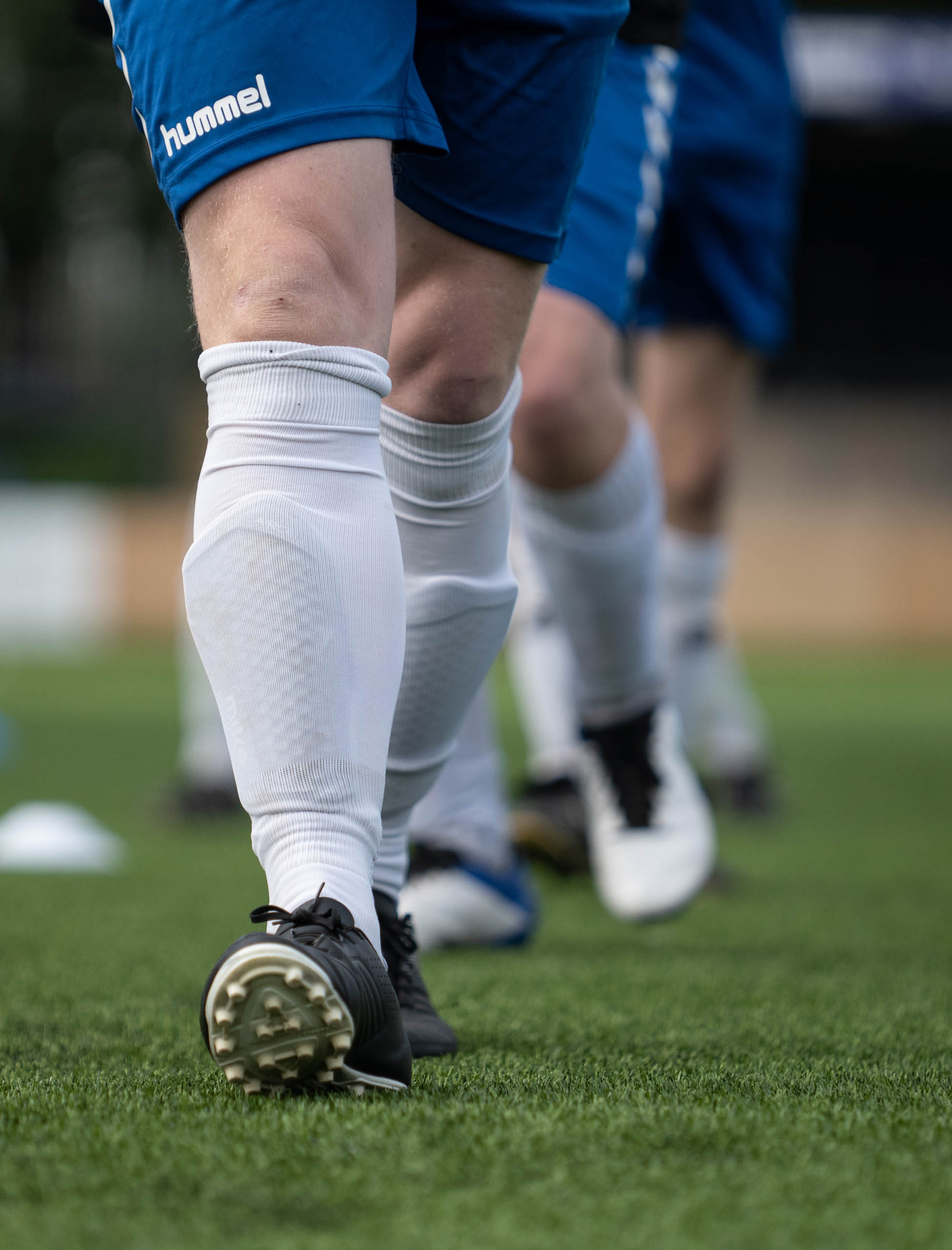 Low-angle close-up of black football boots and white socks as players warm up on artificial turf.