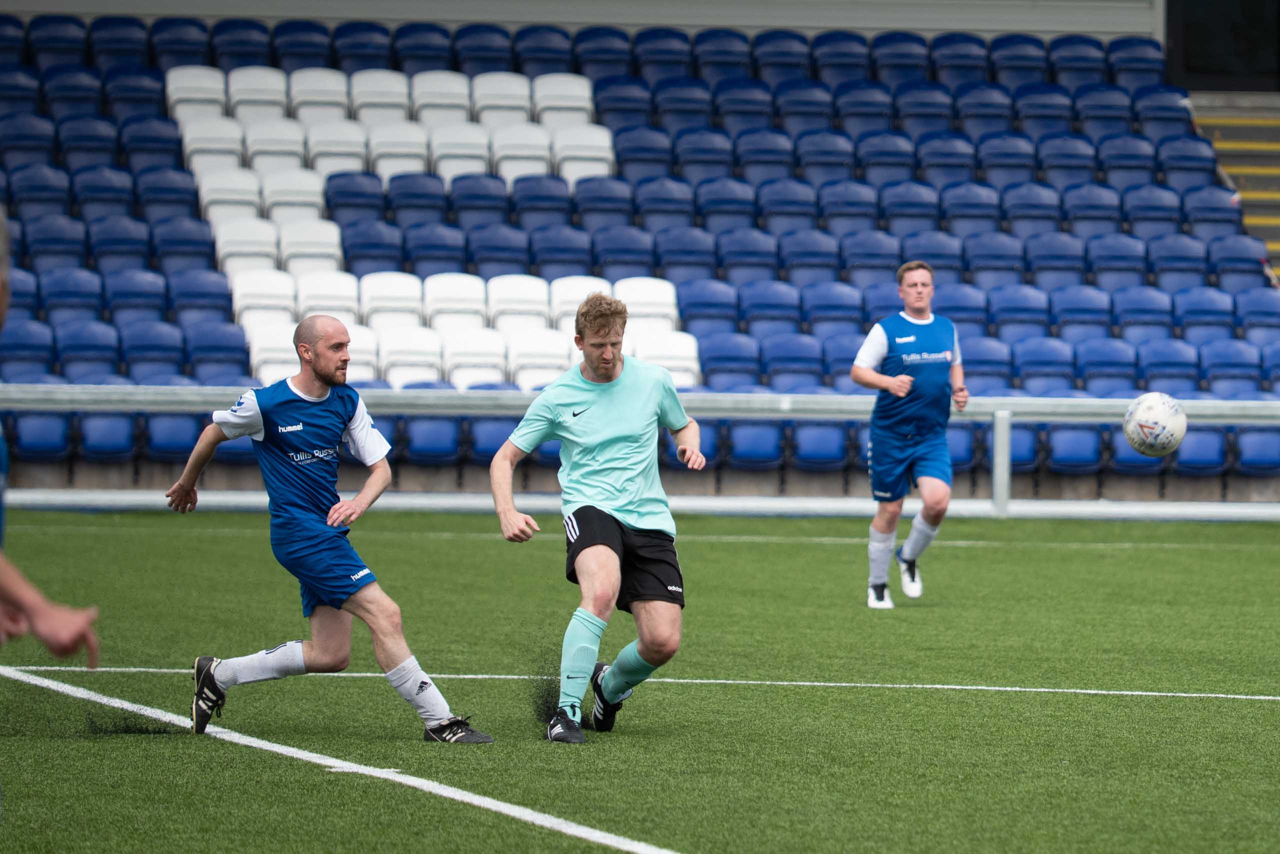 Two amateur footballers battling for possession during a match on artificial grass with teammates in the background.