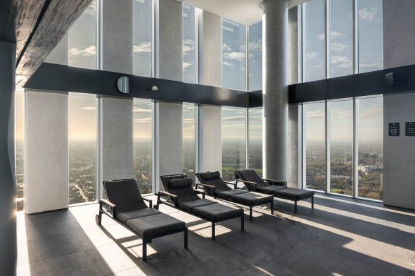 Minimalist spa interior with reclining loungers framed by towering glass walls and sweeping city views.