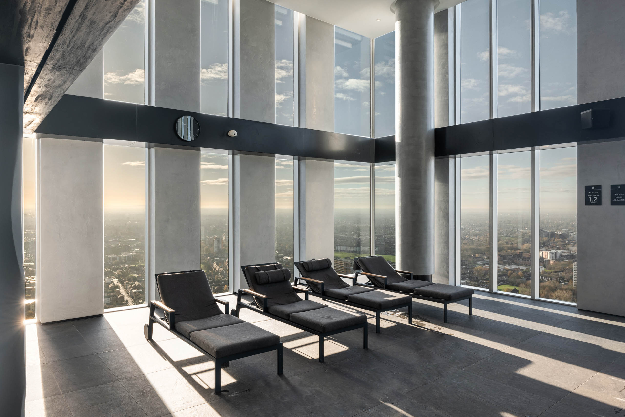 Minimalist spa interior with reclining loungers framed by towering glass walls and sweeping city views.
