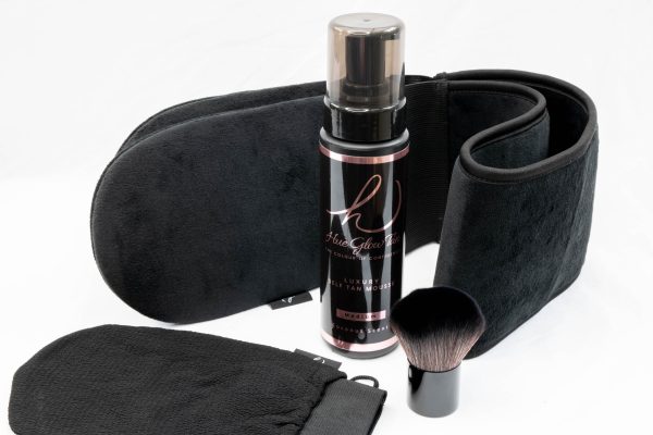Complete self-tanning kit including mousse, mitts, kabuki brush and adjustable waistband displayed on white background.