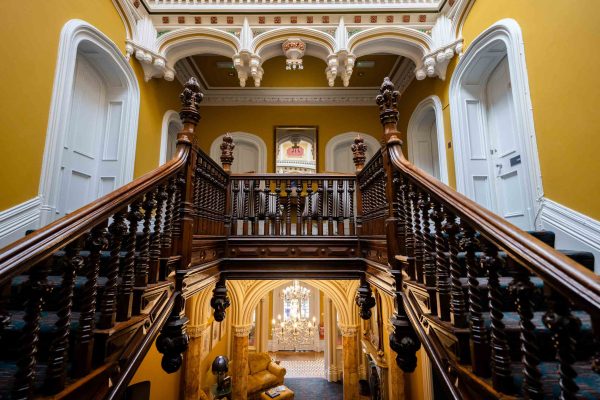 Elaborate wooden staircase in a period home with golden walls and arched architectural features.